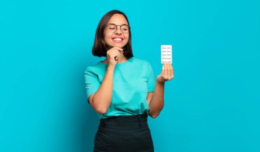 Genç İspanyol kadın mutlu, kendinden emin bir ifadeyle gülümsüyor, çenesinde elleri, merak ediyor ve yan tarafa bakıyor.