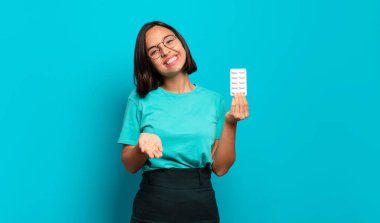 Genç İspanyol kadın mutlu bir şekilde gülümsüyor arkadaş canlısı, kendinden emin, olumlu bakışlı, bir nesne ya da konsept sunuyor ve gösteriyor.