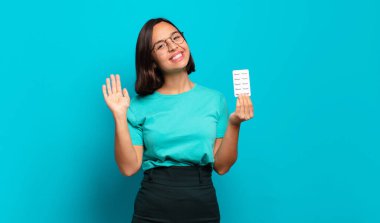 Genç İspanyol kadın mutlu ve neşeyle gülümsüyor, el sallıyor, sizi selamlıyor ya da veda ediyor.