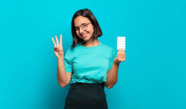 Genç İspanyol kadın gülümsüyor ve arkadaş canlısı görünüyor. Üç ya da üç numarayı gösteriyor. Elleri önde, geri sayıyor.