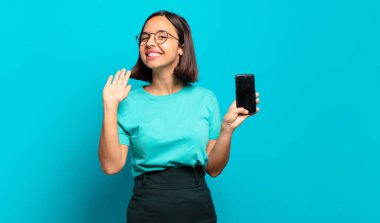 Genç İspanyol kadın mutlu ve neşeyle gülümsüyor, el sallıyor, sizi selamlıyor ya da veda ediyor.