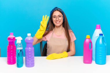 Genç, güzel ev bekçisi gülümsüyor ve arkadaş canlısı görünüyor. Üç ya da üç numarayı gösteriyor. Elleri önde, geriye doğru sayıyor.