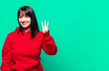 Artı güzel bir kadın gülümsüyor ve arkadaş canlısı görünüyor, üç ya da üç numarayı gösteriyor, eli önde, geriye doğru sayıyor.