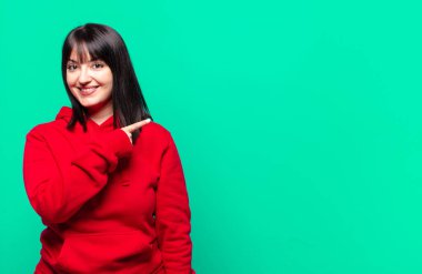 Artı boyut olarak güzel bir kadın neşeli bir şekilde gülümsüyor, mutlu hissediyor ve kenarı ve yukarıyı işaret ediyor, kopya uzayda nesneleri gösteriyor.