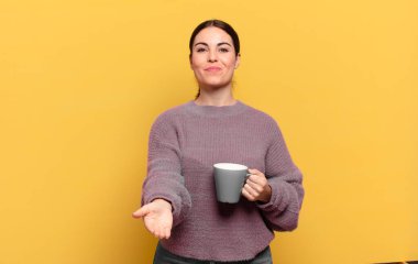 Genç, güzel bir kadın mutlu bir şekilde gülümsüyor. Dost canlısı, kendinden emin, olumlu bakışlı, bir nesne ya da konsept sunuyor ve gösteriyor.