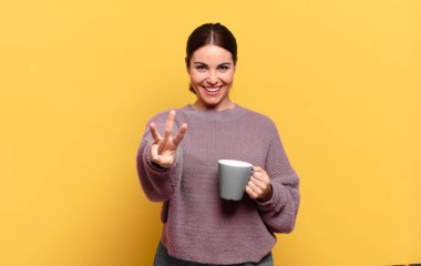 Genç, güzel bir kadın gülümsüyor ve arkadaş canlısı görünüyor. Üç ya da üç numarayı gösteriyor. Elleri önde, geriye doğru sayıyor.