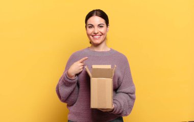 Genç, güzel bir kadın neşeli bir şekilde gülümsüyor, mutlu hissediyor ve kenarı ve yukarıyı işaret ediyor, kopyalama alanında nesneler gösteriyor.