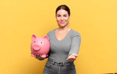 Genç, güzel bir kadın mutlu bir şekilde gülümsüyor. Dost canlısı, kendinden emin, olumlu bakışlı, bir nesne ya da konsept sunuyor ve gösteriyor.