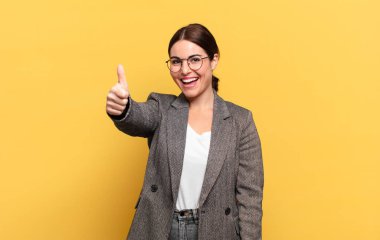 Genç, güzel bir kadın gururlu, tasasız, kendinden emin ve mutlu, başparmağıyla olumlu gülümsüyor.