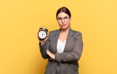 Genç, güzel bir kadın omuz silkiyor, kafası karışık ve kararsız, kolları bağlı ve şaşkın görünüyor.