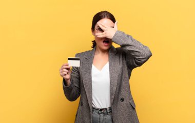 Genç, güzel bir kadın şok olmuş, korkmuş ya da korkmuş görünüyor. Yüzü elle kaplanmış ve parmaklarının arasından gizlice bakıyor.