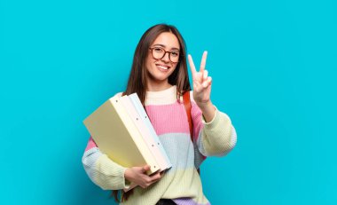 Genç, güzel bir kadın gülümsüyor ve arkadaş canlısı görünüyor. İki ya da iki numarayı gösteriyor. Elleri önde, geri sayıyor.