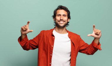 Genç, yakışıklı Hintli bir adam iki eliyle kendi gülüşünü çiziyor, olumlu ve mutlu görünüyor, sağIık kavramı.