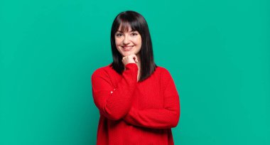 Artı boyda güzel bir kadın mutlu görünüyor ve eli çenesinde gülümsüyor, merak ediyor ya da soru soruyor, seçenekleri karşılaştırıyor.