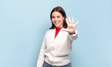 Genç, hoş, sıradan bir kadın gülümsüyor ve arkadaş canlısı görünüyor, 5 ya da 5 numarayı gösteriyor, elleri önde, geriye doğru sayıyor.