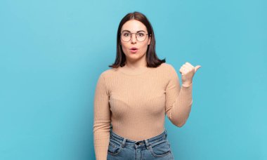 İnançsızlıktan şaşkın şaşkın bakan genç bir kadın yan taraftaki objeyi işaret ederek 