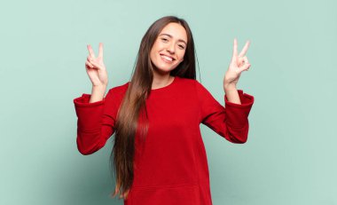 Genç, hoş, sıradan bir kadın gülümsüyor ve mutlu görünüyor, arkadaş canlısı ve tatmin olmuş, zafer ya da barış işareti yapıyor.