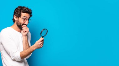 Genç, çılgın, sakallı bir adam büyüteçle arıyor ve bulmaya çalışıyor.