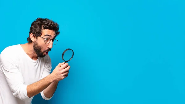 young crazy bearded man looking and trying to find with a magnifying glass