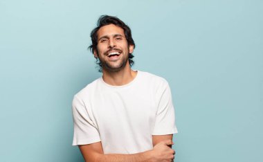 Genç ve yakışıklı Hintli adam utangaç ve neşeli bir şekilde gülüyor, arkadaş canlısı ve olumlu ama güvensiz bir tavırla.