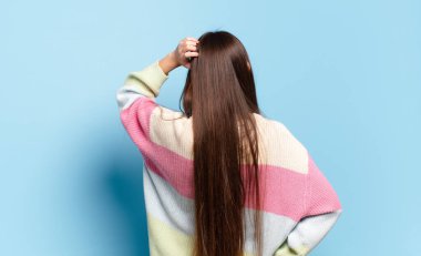 Genç, hoş, sıradan bir kadın, bilgisiz ve kafası karışık, bir çözüm düşünüyor, eli kalçasında, diğeri de kafasında, dikiz aynasından.