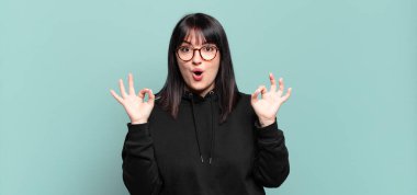 Artı boyut olarak güzel bir kadın şok olmuş, şaşırmış ve şaşırmış hissediyor. Onaylıyor. İki eliyle de onay işareti yapıyor.