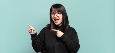 Artı boyut olarak güzel bir kadın, neşeli ve şaşırmış hissediyor, şok olmuş bir ifadeyle gülümsüyor ve yan tarafı işaret ediyor.