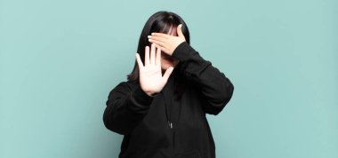 Artı boyda güzel bir kadın yüzünü eliyle kapatıyor ve kamerayı durdurmak için diğer elini öne koyuyor, fotoğraf ya da resimleri reddediyor.