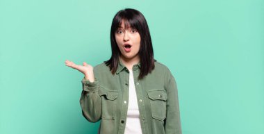 Artı boyut olarak güzel bir kadın şaşırmış ve şok olmuş görünüyor, çenesi düşmüş ve eli açık bir nesneyi tutuyor.