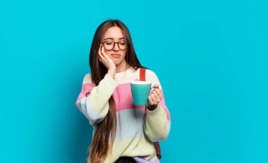 Elinde kahve fincanı olan genç ve güzel bir bayan öğrenci.