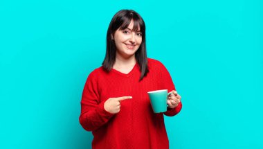 Artı boyut olarak güzel bir kadın neşeli bir şekilde gülümsüyor, mutlu hissediyor ve kenarı ve yukarıyı işaret ediyor, kopya uzayda nesneleri gösteriyor.