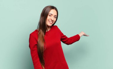 Genç, hoş, sıradan bir kadın mutlu ve neşeli hissediyor, gülümsüyor ve seni hoş karşılıyor, dostça bir jestle içeri davet ediyor.