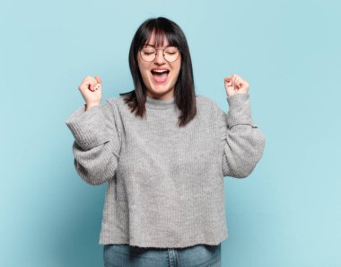 Artı boyut olarak güzel bir kadın çok mutlu ve şaşırmış görünüyor, başarıyı kutluyor, bağırıyor ve zıplıyor.