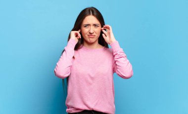 Genç, hoş, sıradan bir kadın sinirli, stresli ve sinirli görünüyor, iki kulağını da sağır edici bir ses, ses ya da yüksek sesle kapatıyor.
