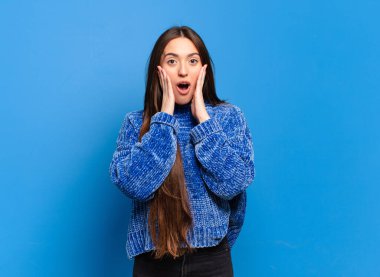 Genç ve hoş bir kadın şok olmuş ve korkmuş hissediyor, ağzı açık ve elleri yanaklarında korkmuş görünüyor.