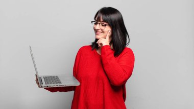 Artı boyut olarak güzel bir kadın mutlu bir şekilde gülümsüyor ve hayal kuruyor ya da şüphe ediyor, yan tarafa bakıyor.