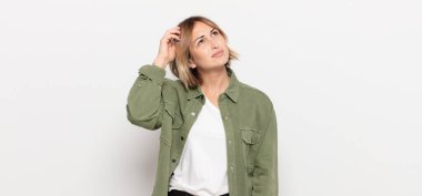 Genç, güzel bir kadın şaşkın ve kafası karışmış hissediyor, başını kaşıyor ve yan tarafa bakıyor.