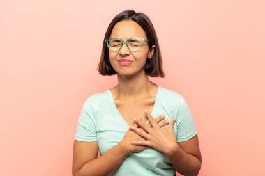 Genç İspanyol kadın üzgün, yaralı ve kalbi kırık görünüyor, iki elini de kalbe yakın tutuyor, ağlıyor ve bunalımda.