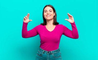 Genç, hoş, sıradan bir kadın. İki eliyle gülücükler çiziyor. Olumlu ve mutlu görünüyor.