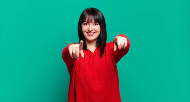 Artı boyut olarak güzel bir kadın mutlu ve kendinden emin hissediyor, kamerayı iki eliyle gösteriyor ve gülüyor, seni seçiyor.