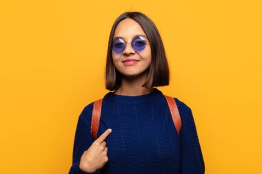 İspanyol kadın gururlu, kendinden emin ve mutlu görünüyor, gülümsüyor ve kendini işaret ediyor ya da bir numara işareti yapıyor.