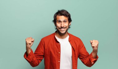 Genç, yakışıklı Hintli adam mutlu, pozitif ve başarılı hissediyor, zaferi, başarıları veya iyi şansı kutluyor.