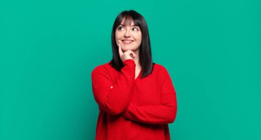 Artı boyut olarak güzel bir kadın mutlu bir şekilde gülümsüyor ve hayal kuruyor ya da şüphe ediyor, yan tarafa bakıyor.