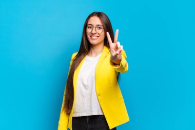 Genç ve güzel bir kadın gülümsüyor ve mutlu görünüyor, kaygısız ve pozitif, zafer ya da barış işareti yapıyor.