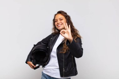 Genç bayan motosiklet sürücüsü mutlu, rahat ve tatmin olmuş hissediyor, iyi bir jestle onaylıyor, gülümsüyor.