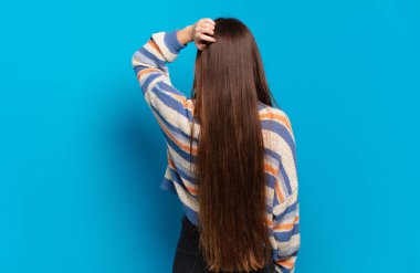 Genç, hoş, sıradan bir kadın, bilgisiz ve kafası karışık, bir çözüm düşünüyor, eli kalçasında, diğeri de kafasında, dikiz aynasından.