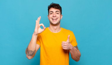 Genç adam mutlu, şaşkın, tatmin olmuş ve şaşırmış hissediyor, iyi görünüyor ve el hareketlerini gösteriyor, gülümsüyor.