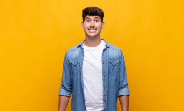 Genç yakışıklı adam mutlu ve şapşal görünüyor. Geniş, eğlenceli, kaçık bir gülüşü ve açık gözleri var.