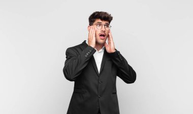 Genç yakışıklı adam mutlu, heyecanlı ve şaşırmış hissediyor, iki eli yüzü yana bakıyor.