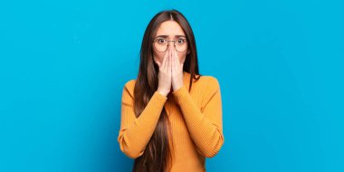 Genç, hoş, sıradan bir kadın endişeli, üzgün ve korkmuş, ağzı ellerle kaplanmış, endişeli ve berbat görünüyor.